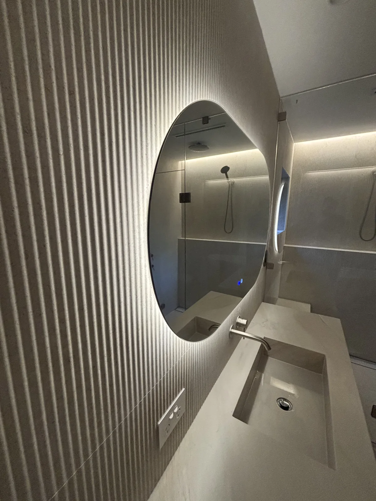 Finished bathroom with a backlit round mirror and fluted feature wall